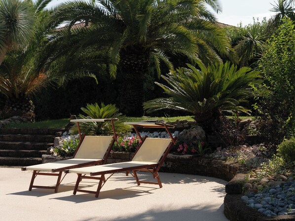 A garden with two wooden lounge chairs and a stone bench.
