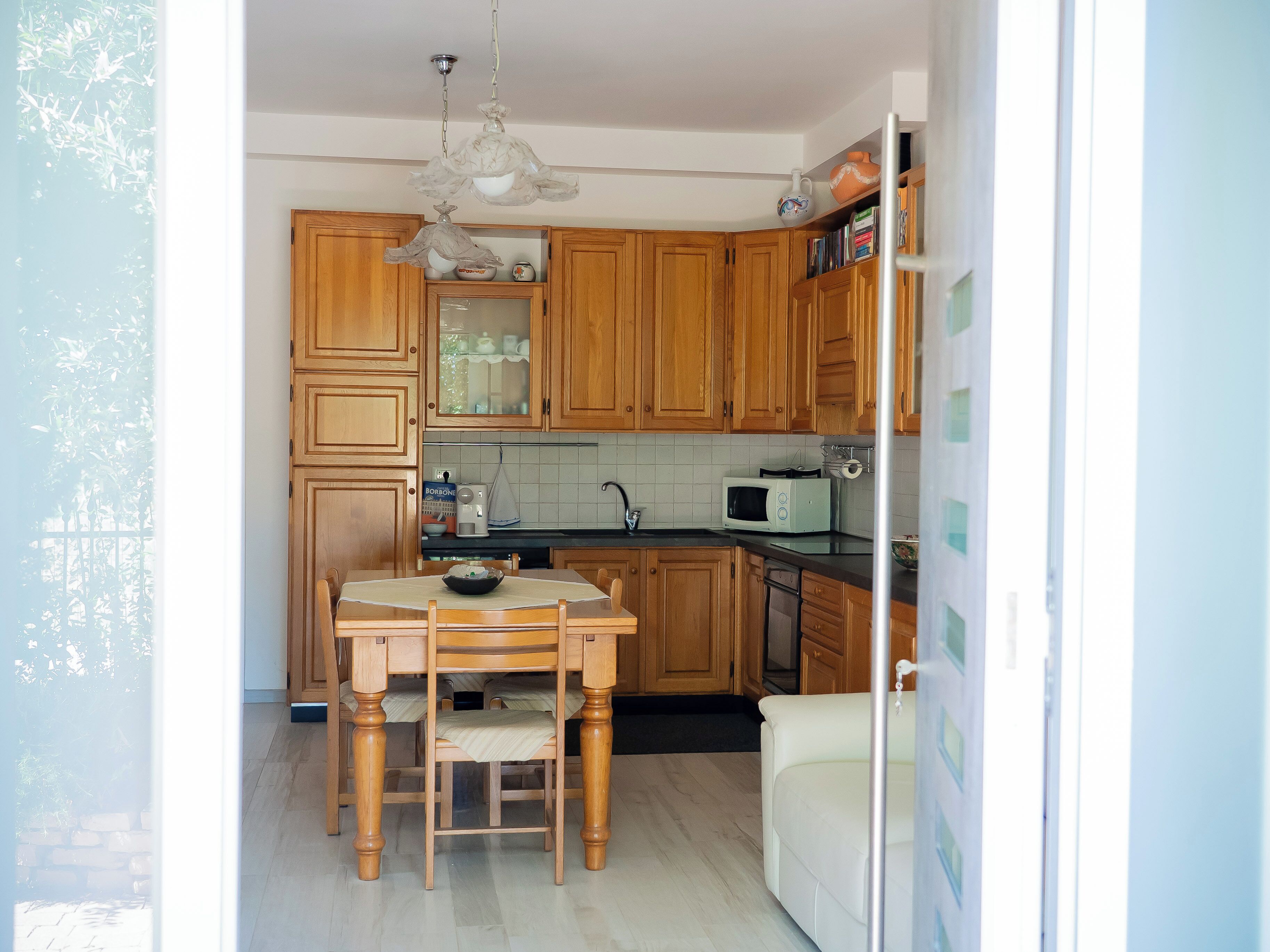 Une cuisine avec des meubles de rangement en bois, une table à manger avec des chaises, un four à micro-ondes et un luminaire suspendu.