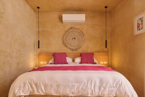 A bedroom with a bed, a wall-mounted air conditioner, a woven wall decoration, and a framed picture on the wall. - Casona Xochimilco - Trinidad (Oaxaca de Juárez)