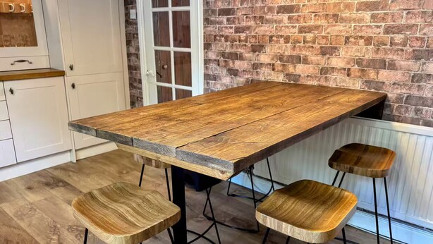 A rustic wooden table with metal legs and three matching stools in a kitchen with white cabinets and a brick wall. - 3 bedroom cottage in the heart of Bingley (Bingley)
