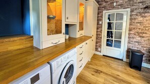 A compact kitchen with wooden countertops, a built-in washing machine, and a brick wall. - 3 bedroom cottage in the heart of Bingley (Bingley)