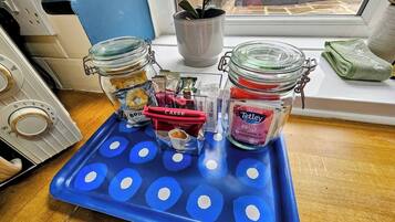 A kitchen counter with a blue tray holding jars of coffee and tea, a kettle, and a plant.