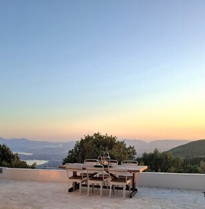 An outdoor dining area with a table and chairs, overlooking a scenic landscape with hills and a body of water. - Villa with sea view (Spartilas)