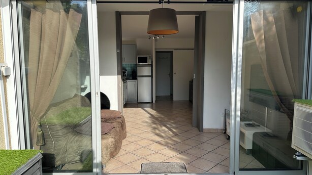 Ein modernes Haus mit einer Schiebetür, die auf eine Terrasse mit bequemen Sitzgelegenheiten und einer kleinen Küche im Hintergrund führt.