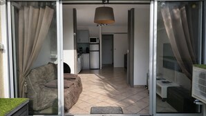 Ein modernes Apartment mit einer Schiebetür zum Balkon, einer Küchenzeile und einem Wohnbereich mit Sofa und Fernseher.