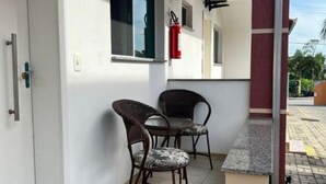 A balcony with two wicker chairs and a small table, a fire extinguisher mounted on the wall, and a door with a handle.