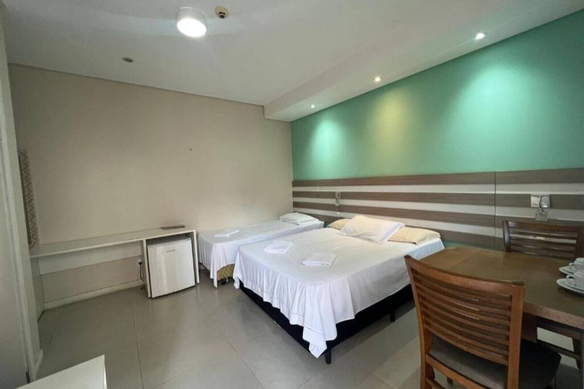 Une chambre d’hôtel avec deux lits simples, un petit bureau, une table avec des chaises et un mur d’accent vert.