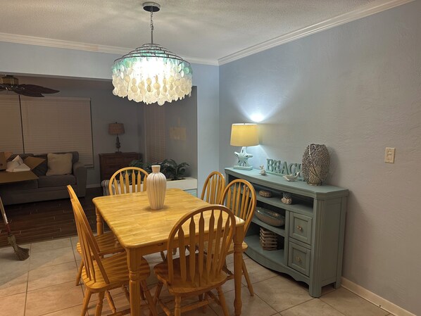 A dining area with a wooden table and chairs, a chandelier, a lamp, and a wall with a 'BEACH' sign. - 2-bedroom house in lovely Seminole near lots of outdoor recreation! (Seminole)
