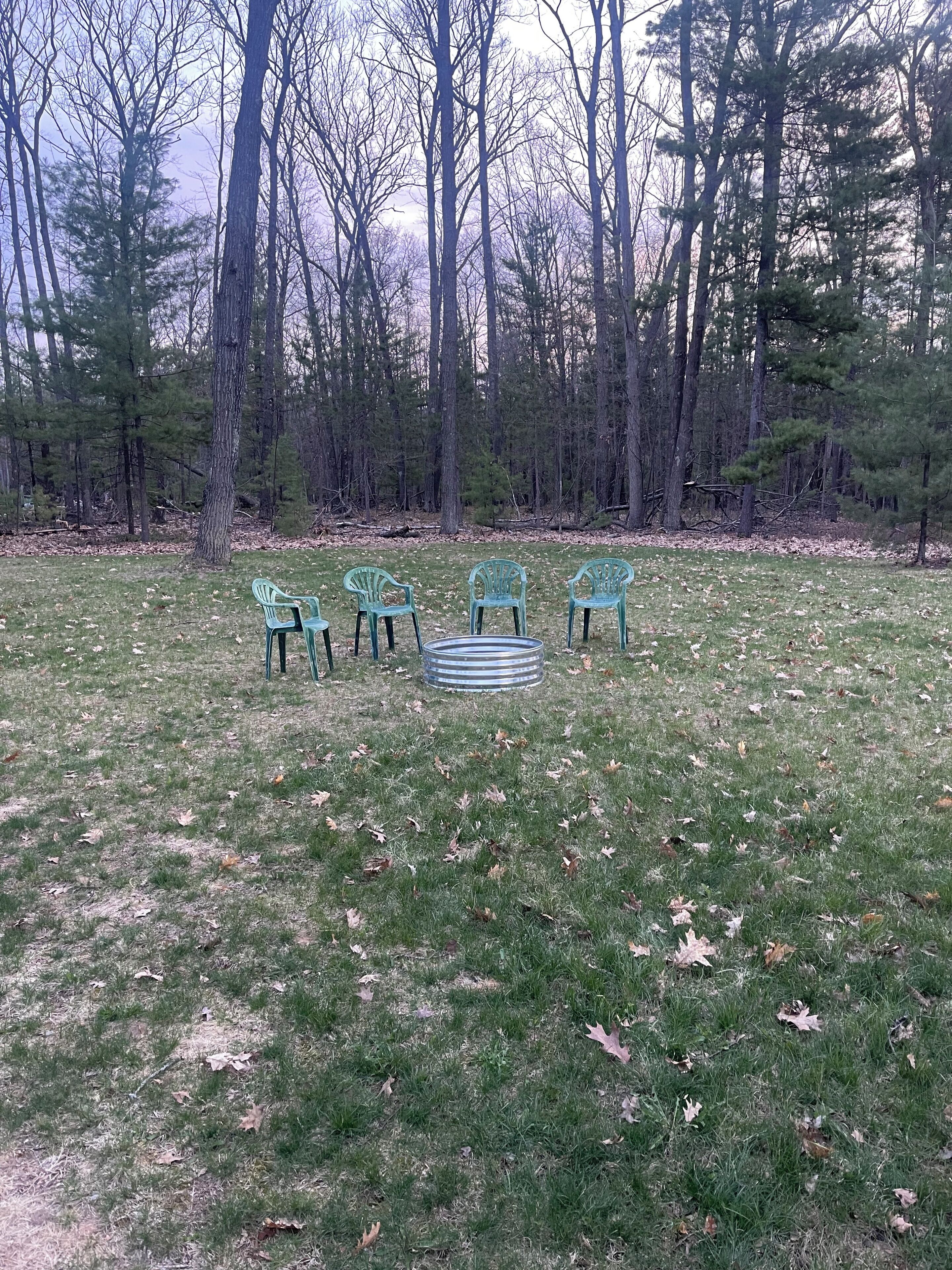 A grassy outdoor area with four green chairs and a striped metal table.