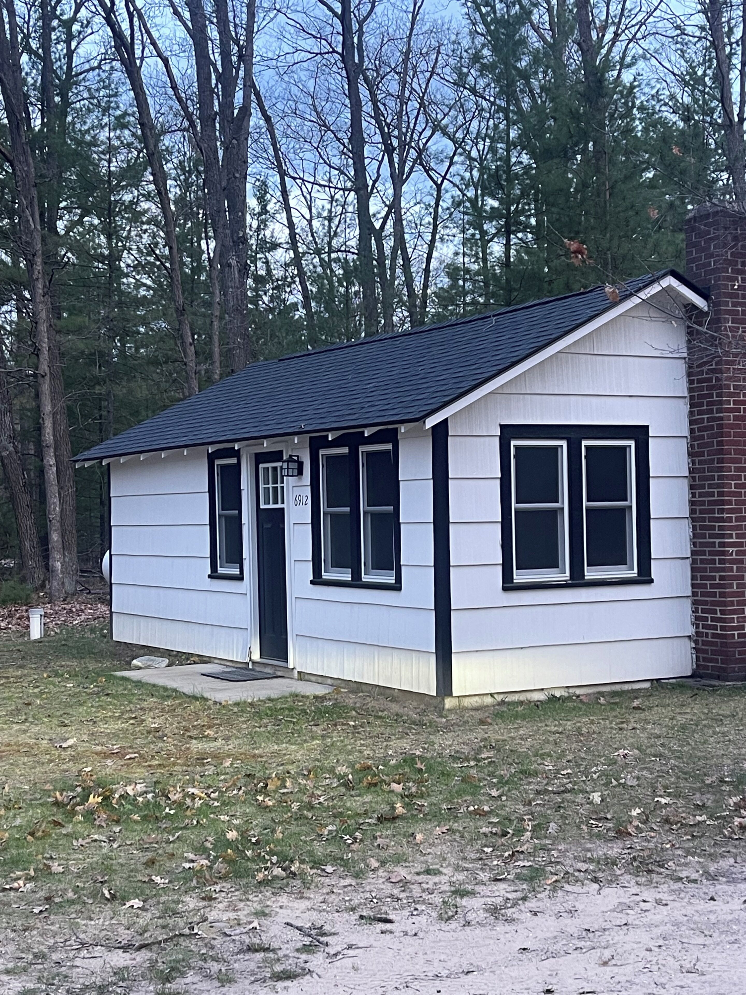 A small, single-story building with a dark roof and white siding, surrounded by trees.