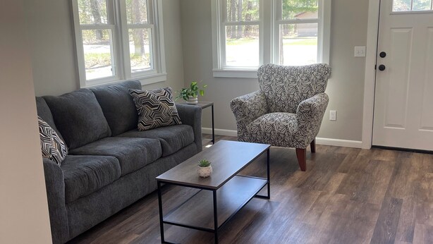 A living room with a gray sofa, a patterned armchair, a small table, and a door.