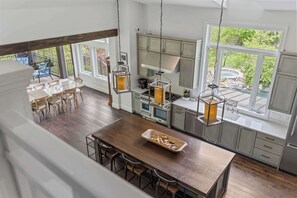 Een keuken met een centraal eiland, een houten eettafel en stoelen, met grote ramen met uitzicht op groen en een hottub.