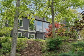 Een modern huis met twee verdiepingen, grote ramen, omringd door bomen en een tuin.