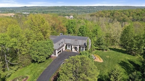 A large house with a driveway, surrounded by trees and a hilly landscape.