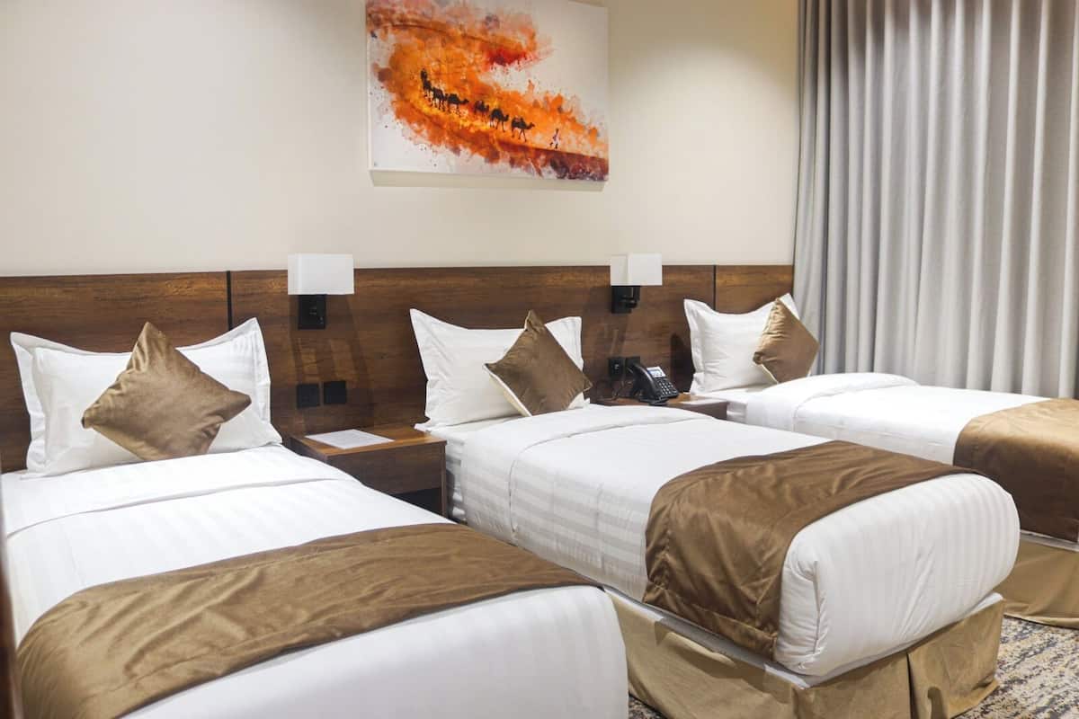 A hotel room with three single beds, a wooden headboard, a painting on the wall, and a telephone on the nightstand.