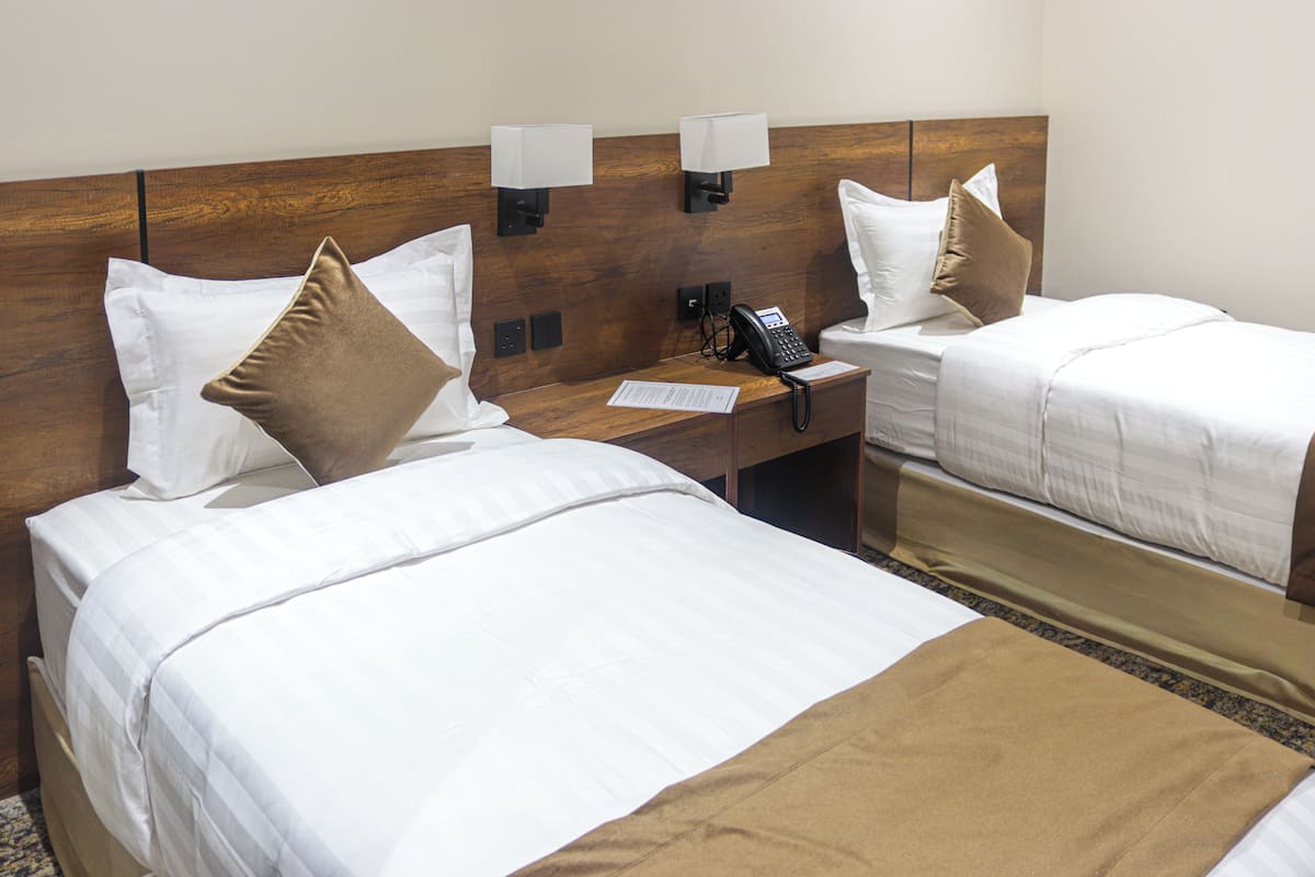 A hotel room with two beds, a wooden headboard, bedside lamps, a telephone, and a notepad on the nightstand.