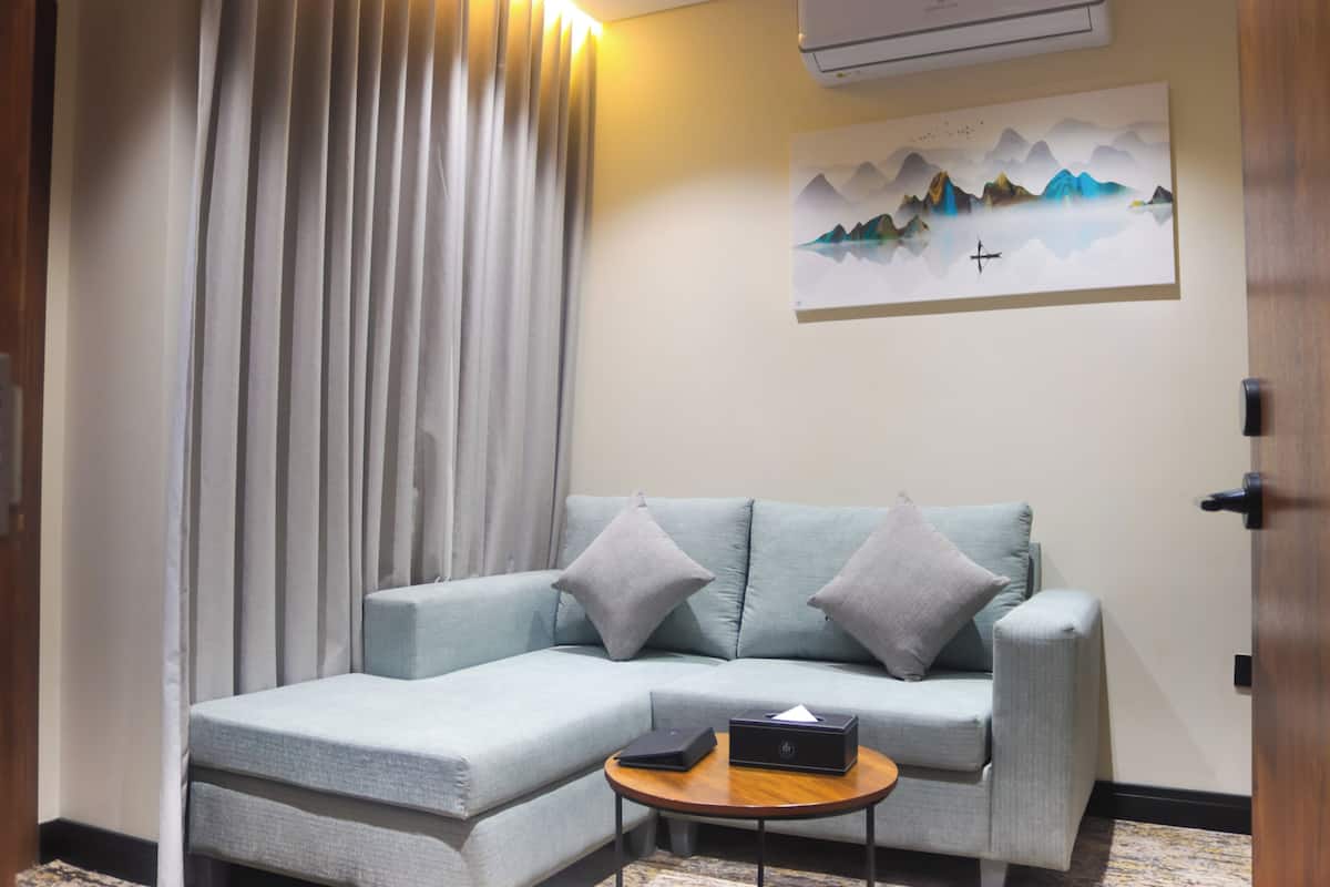 A modern living room with a light blue sectional sofa, a small wooden coffee table, and a painting of mountains on the wall.