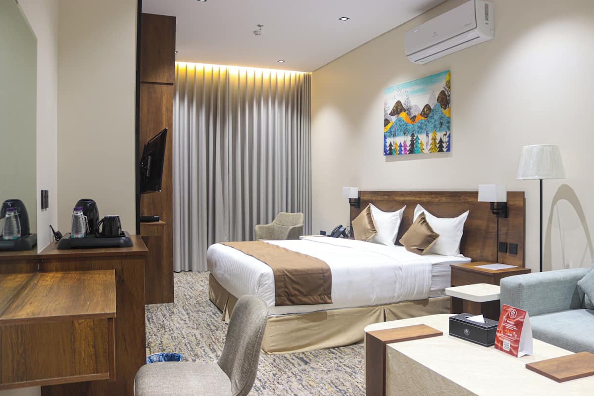 A hotel room with a bed, desk, chair, and a painting on the wall.