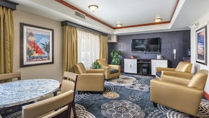 A hotel room with a round marble table, two sofas, a television, and a cabinet.