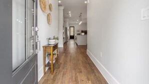A modern hallway with wooden flooring, a small table with a plant, and decorative wall art. - Serene Beach Oasis with Heated Pool (Biloxi)