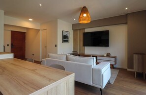Ein modernes Wohnzimmer mit einem Holzespeisetisch, weißen Sofas, einem an der Wand montierten Flachbildfernseher und einer hölzernen Deckenleuchte.