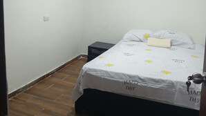 Ein kleiner, einfach eingerichteter Raum mit einem Einzelbett, einem kleinen Nachttisch und einem Fenster mit heruntergelassenen Jalousien.