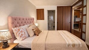 Ein Schlafzimmer mit einem gepolsterten Kopfteil, einem Bett mit einer beige farbenen Decke, einer Nachttischlampe und einem Holzschrank.