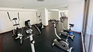 Une salle de sport équipée de plusieurs vélos d’appartement et de plusieurs appareils elliptiques, avec un sol noir, des murs blancs et un plafond agrémenté d’un luminaire.