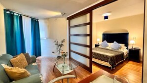 Une chambre d’hôtel comprenant un lit, des tables de chevet, un canapé, une table basse en verre et une vue accessible par une porte coulissante.