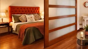 Ein Schlafzimmer mit einer gepolsterten Kopfteile, einem Bett mit vielen Kissen, einem Nachttisch mit Lampe und einer schiebbaren Holzwand.