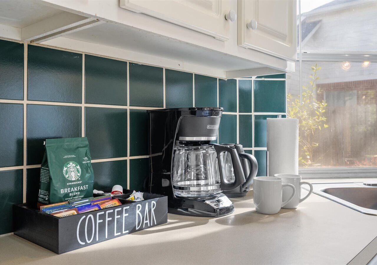 Une cuisine aménagée avec un coin café, comprenant une machine à café, un sac Starbucks et une boîte étiquetée « COIN CAFÉ ».