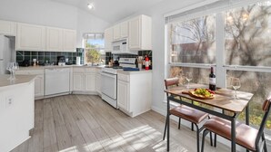 Una cucina moderna con mobili bianchi, un tavolo da pranzo in legno e un'ampia finestra con vista sull'esterno.