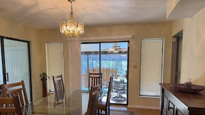 Un coin repas avec une table en verre, des chaises en bois, un lustre et une vue sur un balcon agrémenté d’une balustrade.