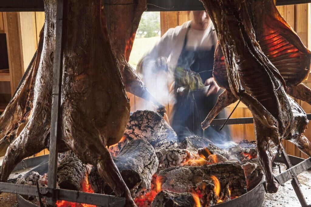 A traditional outdoor cooking setup with a fire pit and hanging meat.