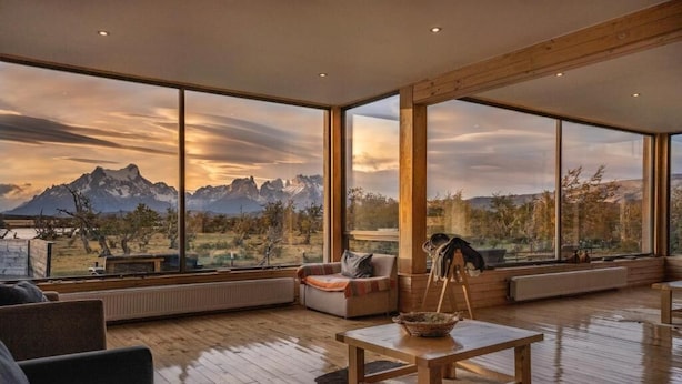 Un amplio salón con ventanas grandes que ofrecen vistas a la montaña, una mesa de madera y asientos cómodos.