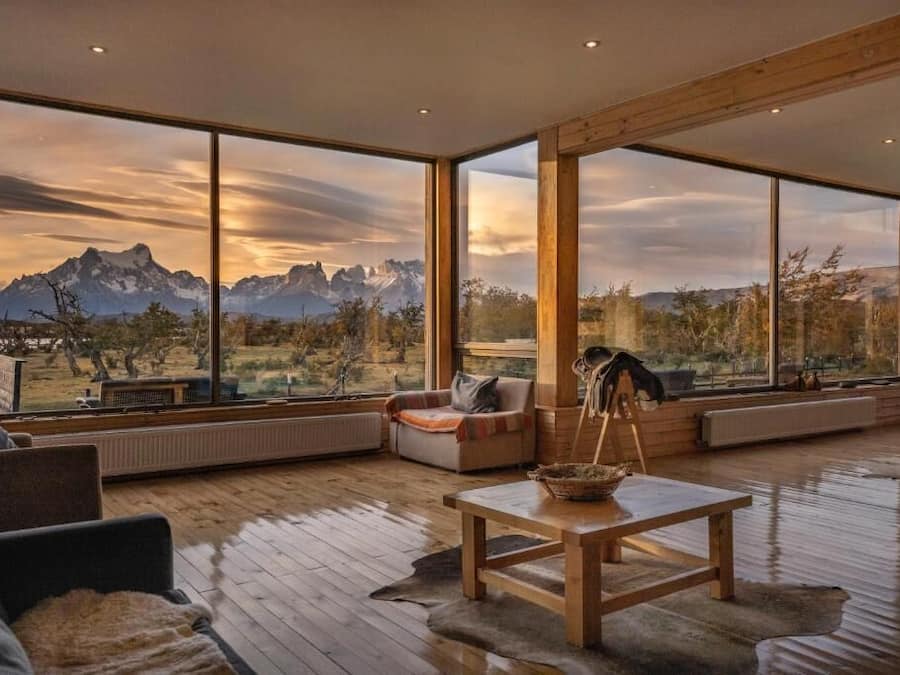 A spacious living room with large windows offering a mountain view, a wooden table, and comfortable seating.