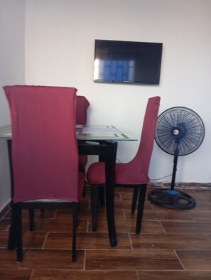 A dining area with a table and chairs, a wall-mounted TV, and a standing fan. - Refresh yourself with the best view of the sea and the main dock of the port. (Puerto Colombia)