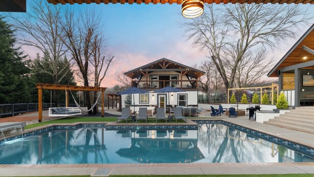 Una casa moderna con piscina, mobiliario exterior y una pérgola.