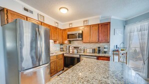 A modern kitchen with granite countertops, stainless steel appliances, wooden cabinets, and a window with blinds. - NEW, Large 2BR in Ocean Greens,Great Location,Pool (North Myrtle Beach)