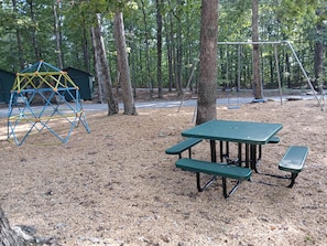 Een speeltuin met een klimconstructie en picknicktafels in een bebost gebied.