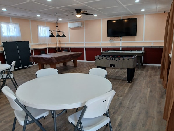 Una habitación con mesa de billar, mesa de futbolín y televisor instalado en la pared.