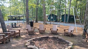 Un camping con sillas de madera, un brasero, mesas de picnic y un conjunto de columpios.