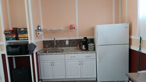 Una cocina compacta con armarios blancos, un microondas integrado, una cafetera y un refrigerador blanco.
