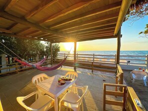 A beachside patio with a table set for two, a hammock, and a view of the ocean at sunset.
