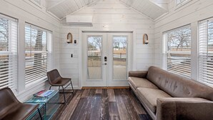 A cozy room with a wooden ceiling, a ceiling fan, a brown leather sofa, a glass coffee table, and large windows with blinds. - The Resort at Fredericksburg Unit 1 (Fredericksburg)