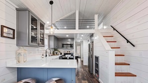 A kitchen with a central island, bar stools, a staircase, and a hanging light fixture. - The Resort at Fredericksburg Unit 1 (Fredericksburg)