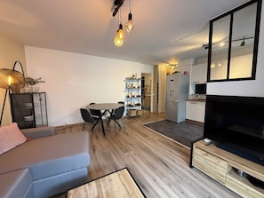A modern living room with a sofa, a TV, a dining area with chairs, a kitchen with cabinets, and a staircase leading to another level. - Modern apartment with terrace - ideal location (Cagnes-sur-Mer)