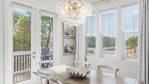 Un espace repas avec une table et des chaises blanches, un élément décoratif au centre, et une vue dégagée grâce à de grandes fenêtres.