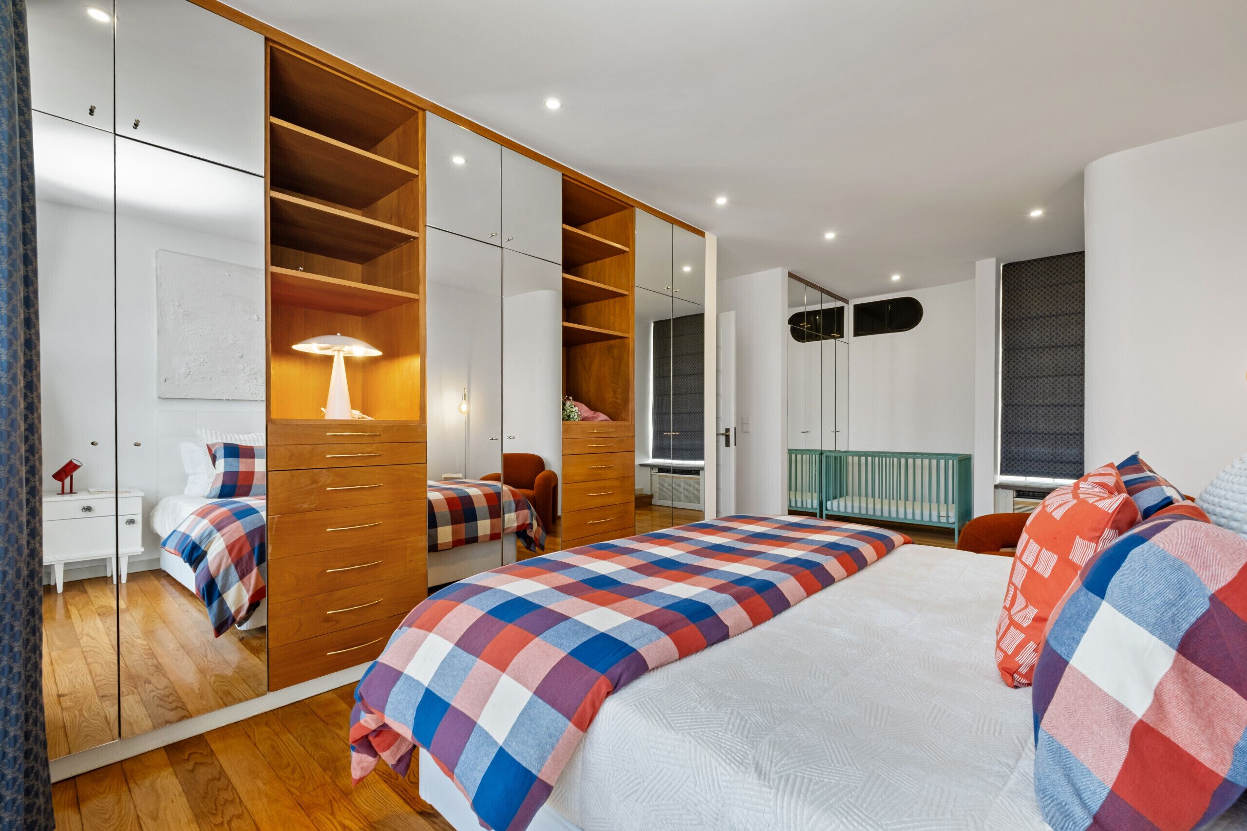 A bedroom with a large bed, a wardrobe with mirrored doors, a bedside table, and a lamp.
