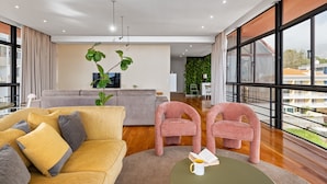 Ein modernes Wohnzimmer mit einer Couch, zwei Sesseln, einem Couchtisch und einem großen Fenster mit Blick auf Gebäude.